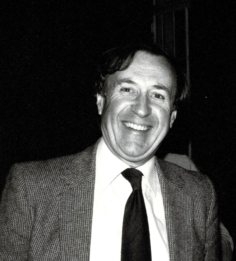 Black and white photo of a smiling and suited Rex Mason in 1984