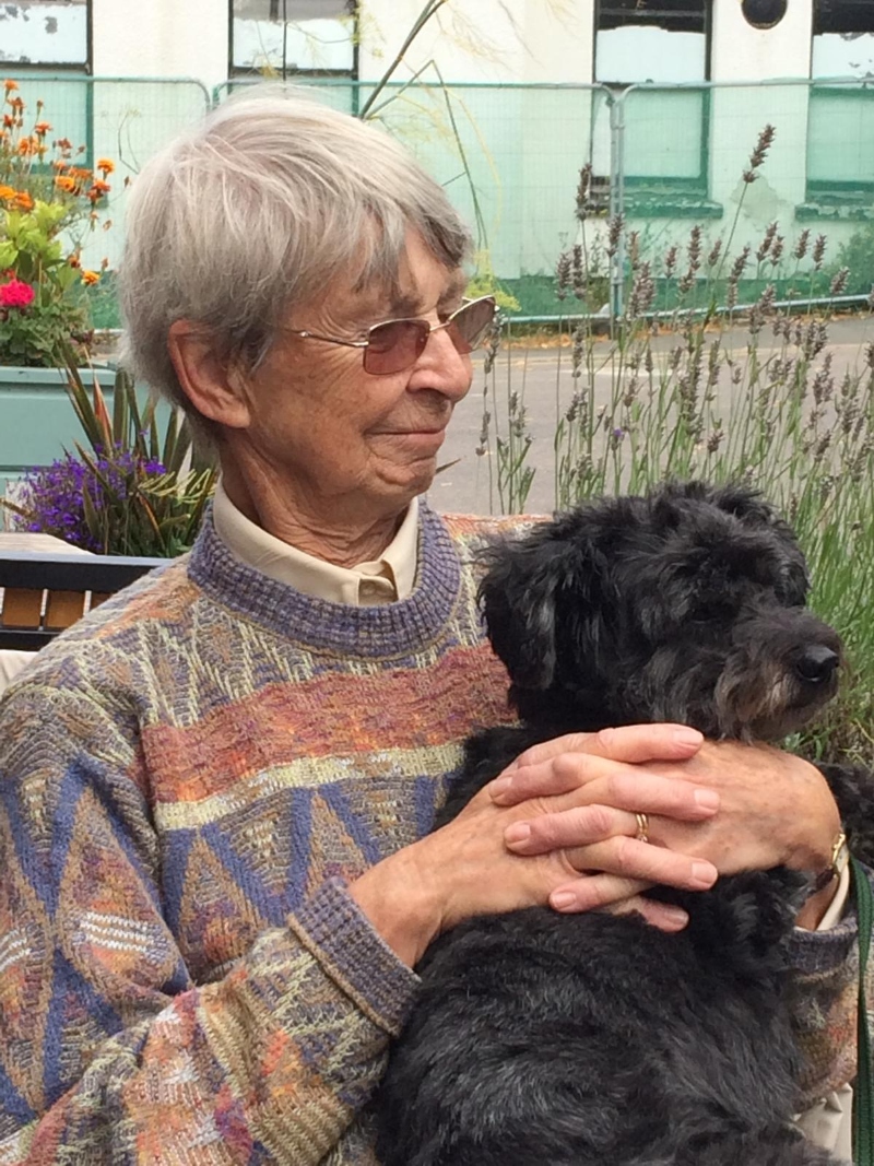 The Revd Pat Heap, holding and looking at a small black dog