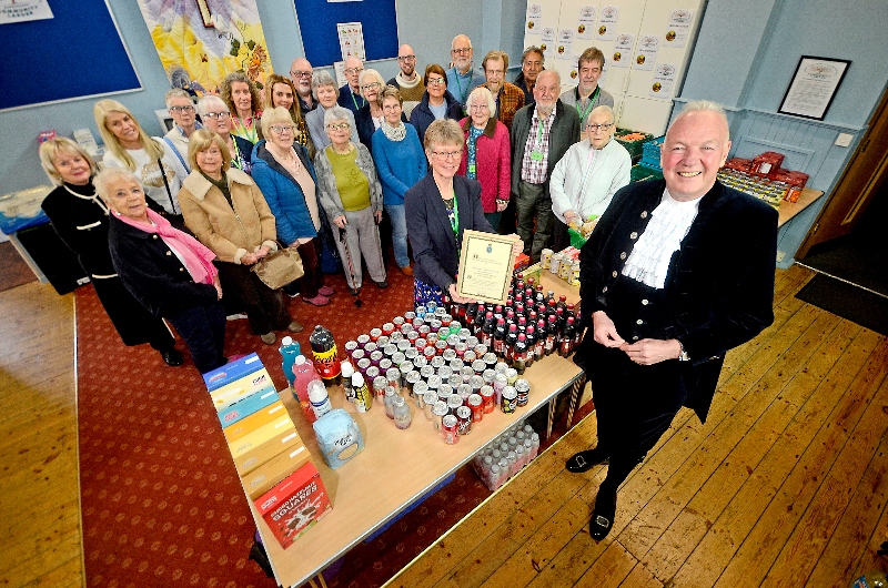 The High Sheriff stands in front of a table of food. Behind him are the Alvechurch larder volunteers, stood in a semi circle