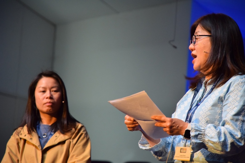 Sharon Shek and Londy Chan on stage, with Londy speaking, and Sharon looking on