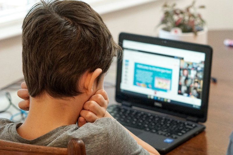 Back of a boy's head, showing him looking at laptop screen, hands on his neck indicating nervousness