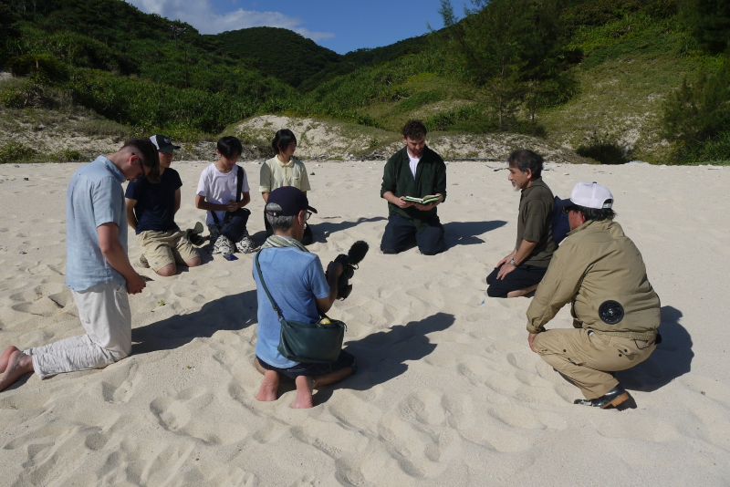 Akijima beach - several people kneel in a circle while one of the group reads from the Bible