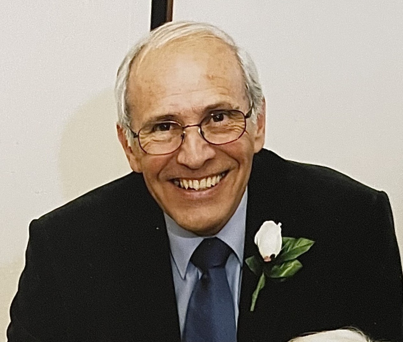 Martin Mitchell, wearing a dark suit and blue tie, smiling