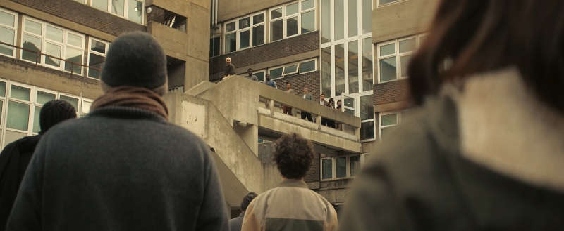 A scene from Testament, filmed in London, in which a diverse group of people stands together in front of a large block of flats