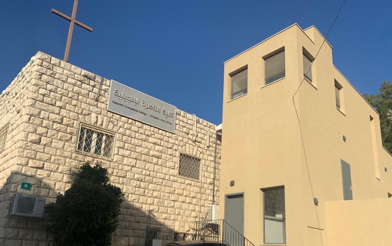 Picture of exterior of Nazareth Evangelical College, showing its extension against a bright blue sky. A Christian cross sits prominently at the top of the building