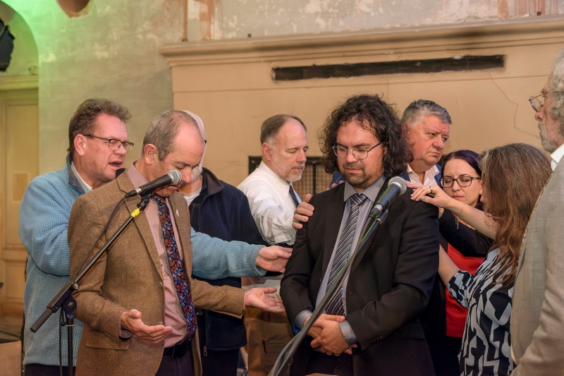 David Bunce stands in the middle of around 8 people with head bowed as he is prayed for 
