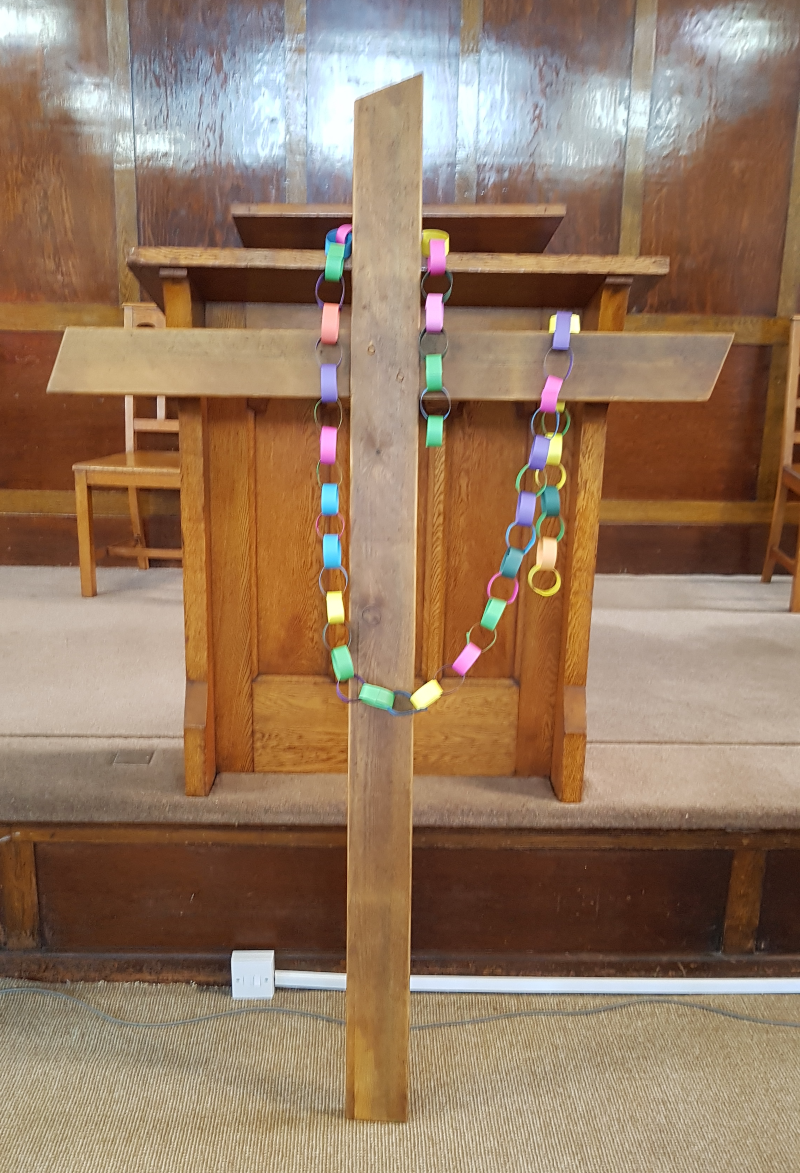 A colourful paper chain is hung over a wooden cross at the front of a church
