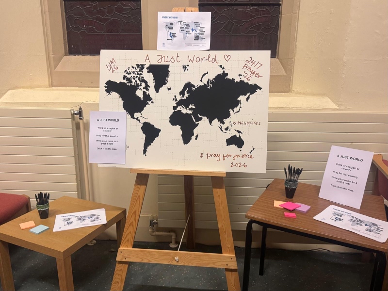 An interactive "A Just World" prayer station featuring a large world map display with sticky notes and pens on nearby tables.