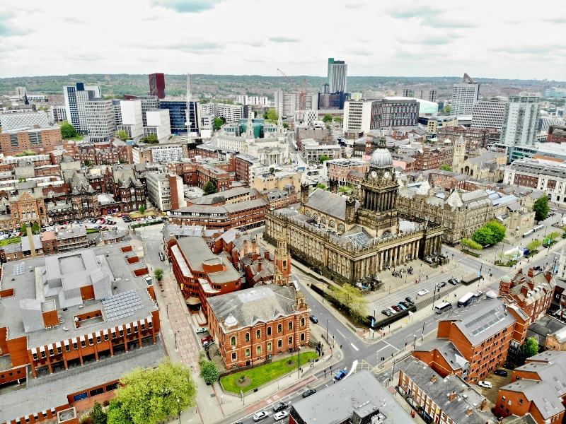 An aerial high-angle view of the Leeds city skyline, prominently featuring Leeds Town Hall surrounded by streets, modern office buildings, and historic architecture