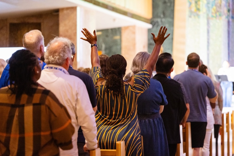 Baptist World Alliance worship 2026: A congregation standing in worship during a church service, viewed from behind, with one woman raising both hands in praise